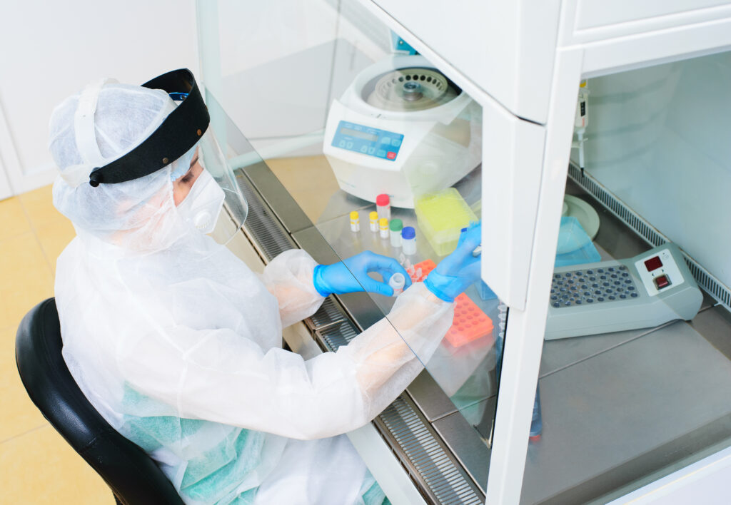 female pcr laboratory researcher in a protective medical suit, sterile mask, helmet, rubber gloves with a dispenser in her hands