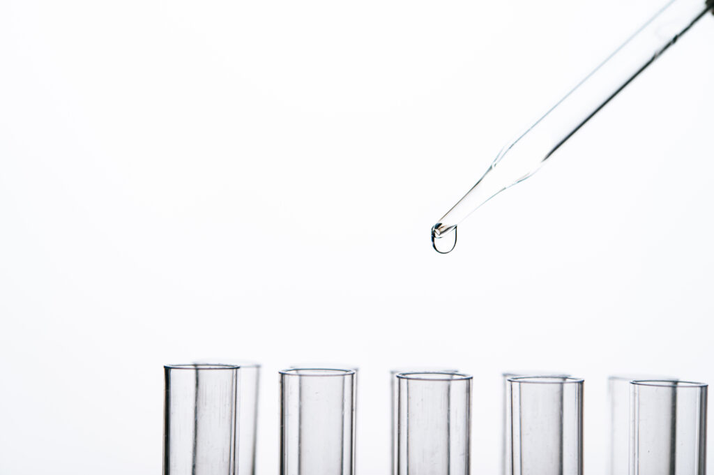 Glass Pasteur pipette dropper releasing a liquid droplet above a row of laboratory test tubes.