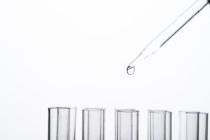 Glass Pasteur pipette dropper releasing a liquid droplet above a row of laboratory test tubes.